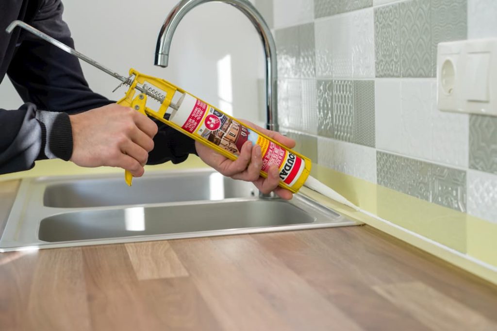 builder applying adhesive in seam between wall tiles and kitchen counter