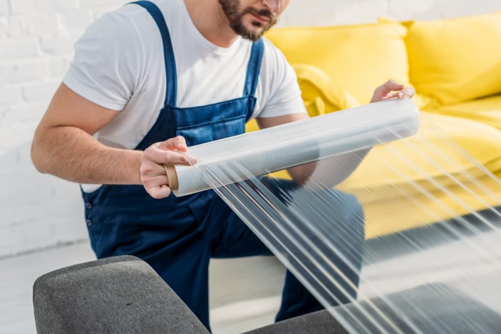 man packaging furniture with plastic protective wrap