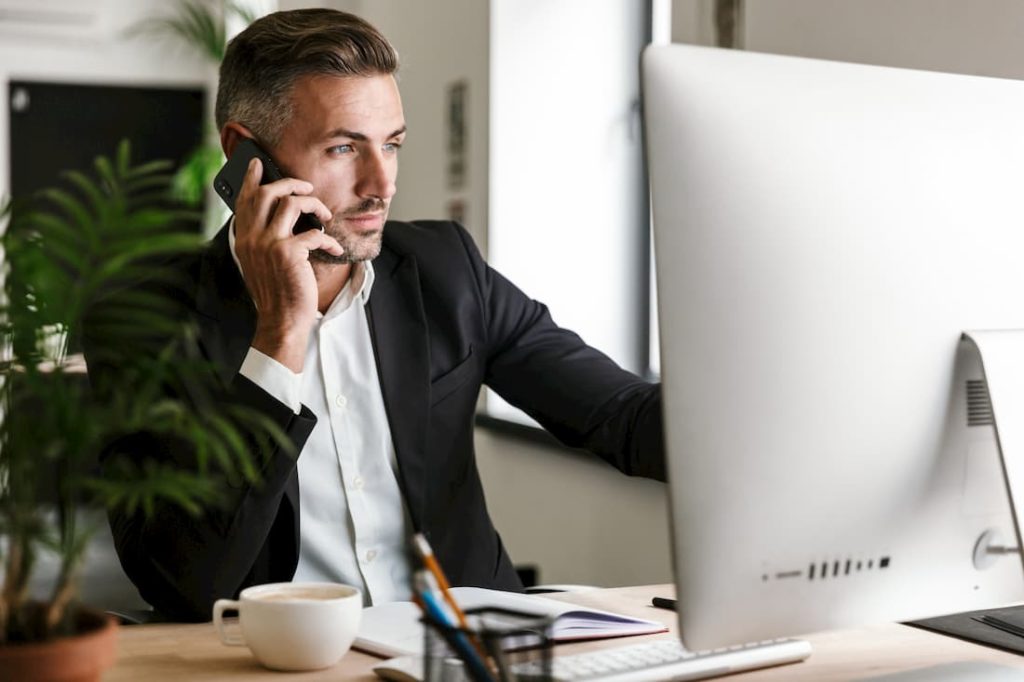 business specialist in product sourcing using mobile phone looking at computer screen