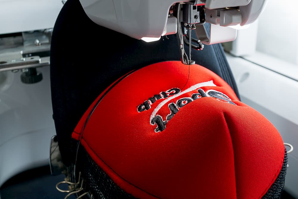 Close up image of red and black sport cap finish embroidering on the hoop of white embroidery machine