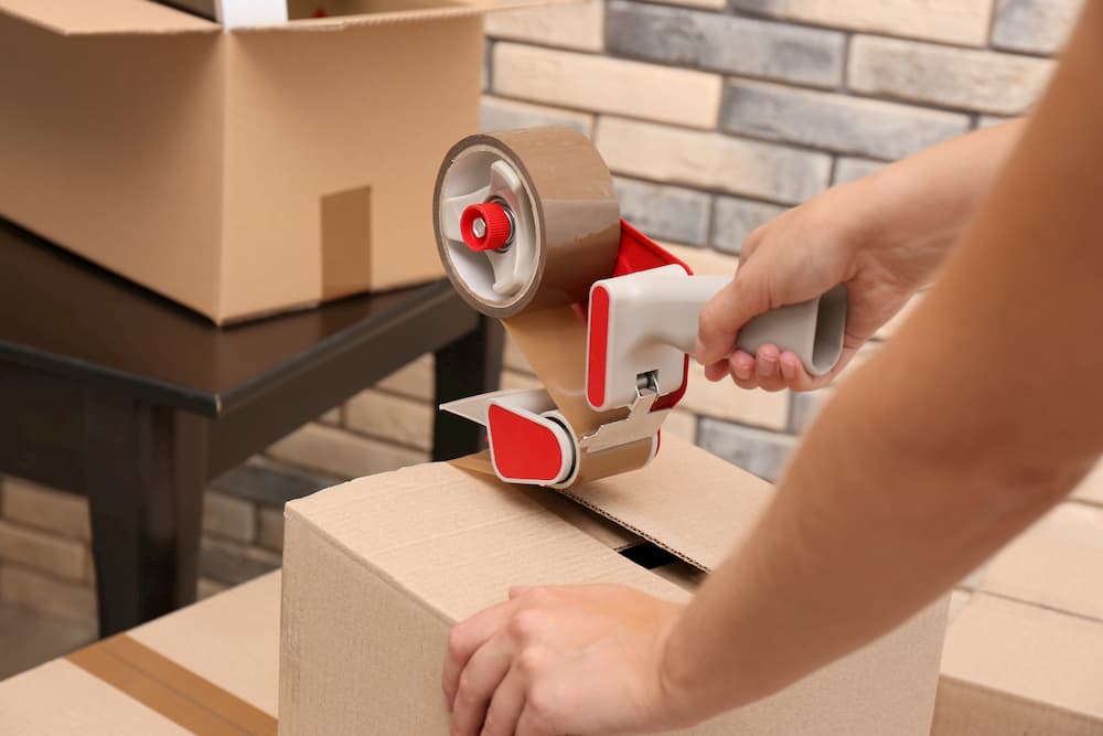 Woman packing carton box indoors, closeup. Moving day